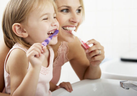 Mother And Daughter Brushing Teeth Together Over Sink