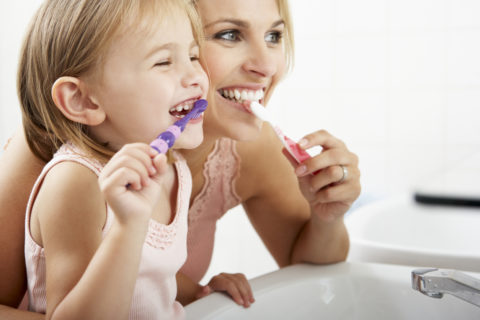 Mother And Daughter Brushing Teeth Together Over Sink